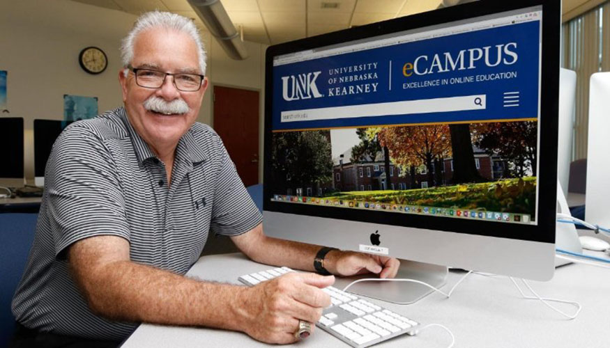 Man sitting next to mac computer showing UNK website